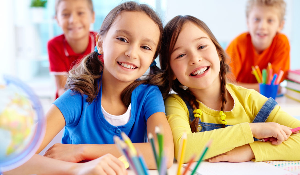 Zwei Mädchen sitzen in einer Schulklasse und lächeln in die Kamera